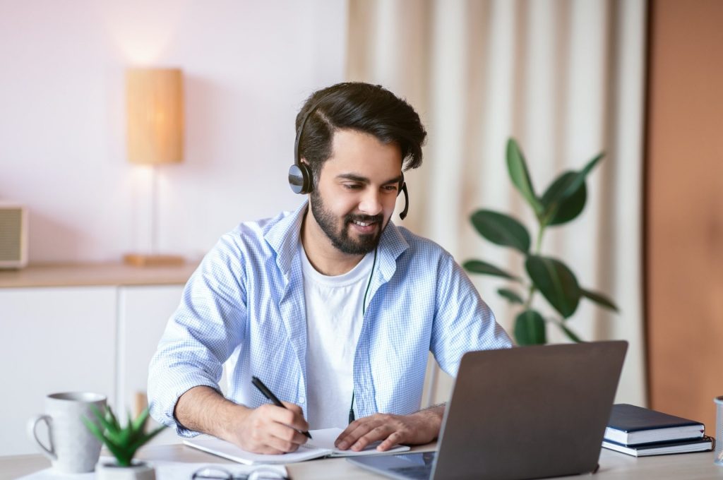 Online Education. Young Arab Guy Watching Webinar On Laptop And Taking Notes
